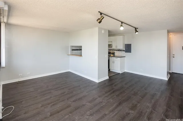 a view of empty room with wooden floor and kitchen