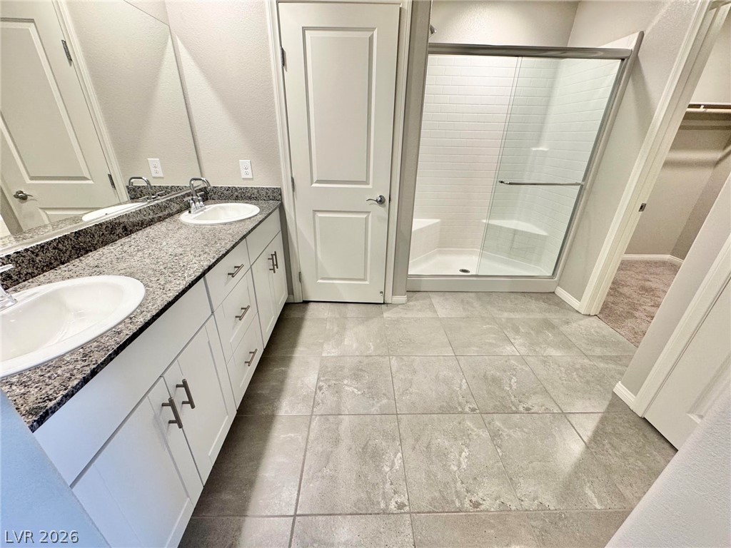 7020 Colonial Ranch Street Las Vegas, NV 89166 - Photo 12 of 37 Tiled flooring pairs with a long double vanity and a glass-enclosed walk-in shower.