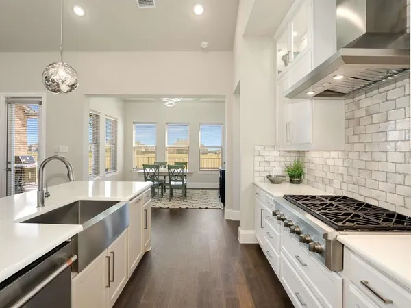 a large kitchen with stainless steel appliances a stove a sink dishwasher a dining table and chairs with wooden floor