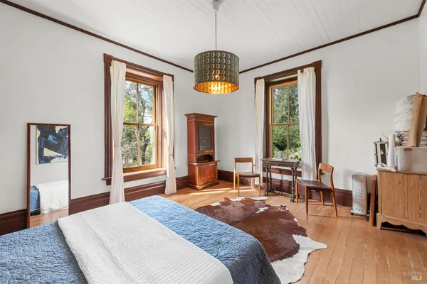 a spacious bedroom with a bed a large window and wooden floor
