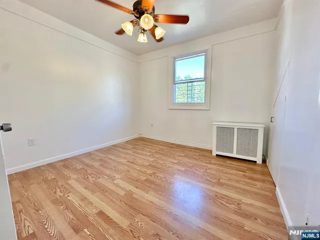 an empty room with wooden floor chandelier fan and windows