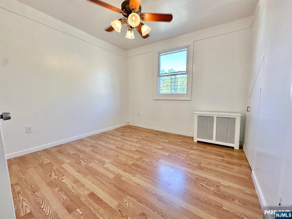 23 Trimble Avenue, Unit 2 Clifton, NJ 07011 - Photo 6 of 16 an empty room with wooden floor chandelier fan and windows