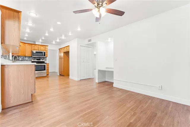 an empty room with wooden floor kitchen view and windows