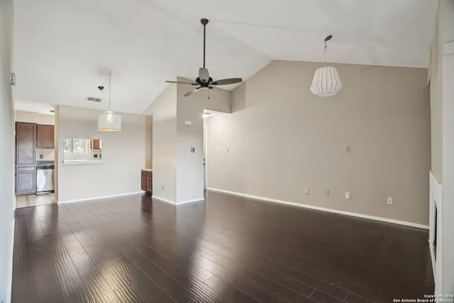 a view of an empty room with wooden floor and a kitchen