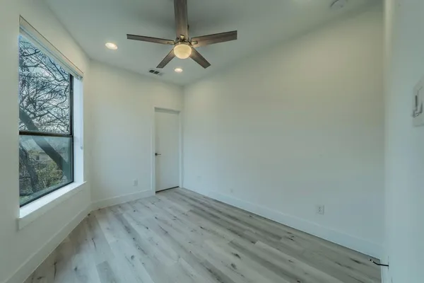 an empty room with wooden floor fan and windows