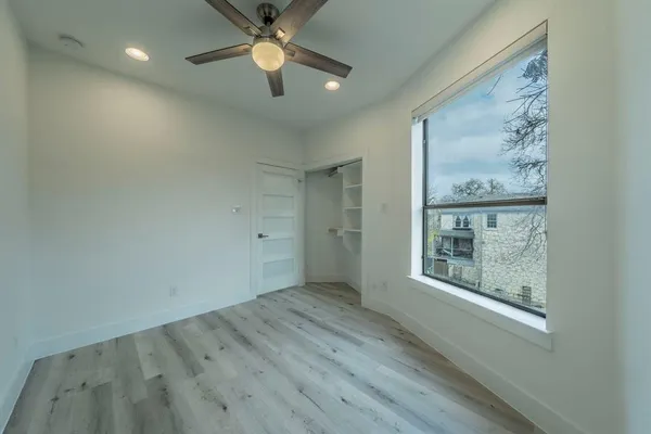an empty room with wooden floor chandelier fan and windows