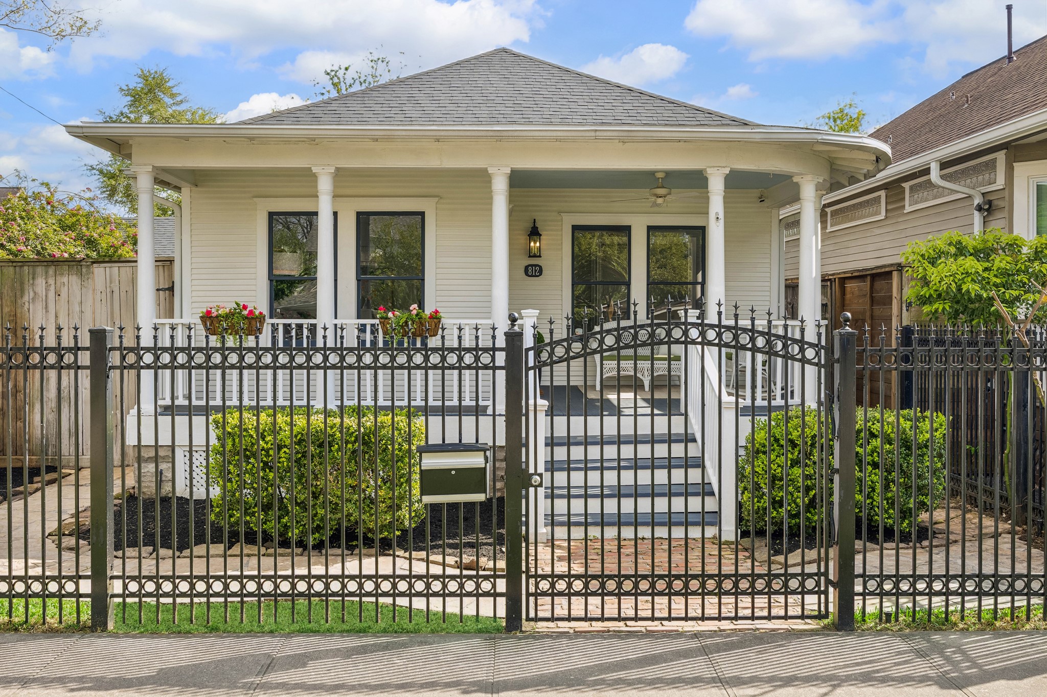 Charming single-story home with a welcoming front porch, classic columns, and a neatly landscaped yard. Features a decorative iron fence and a pathway leading to the entrance, offering both privacy and curb appeal.
