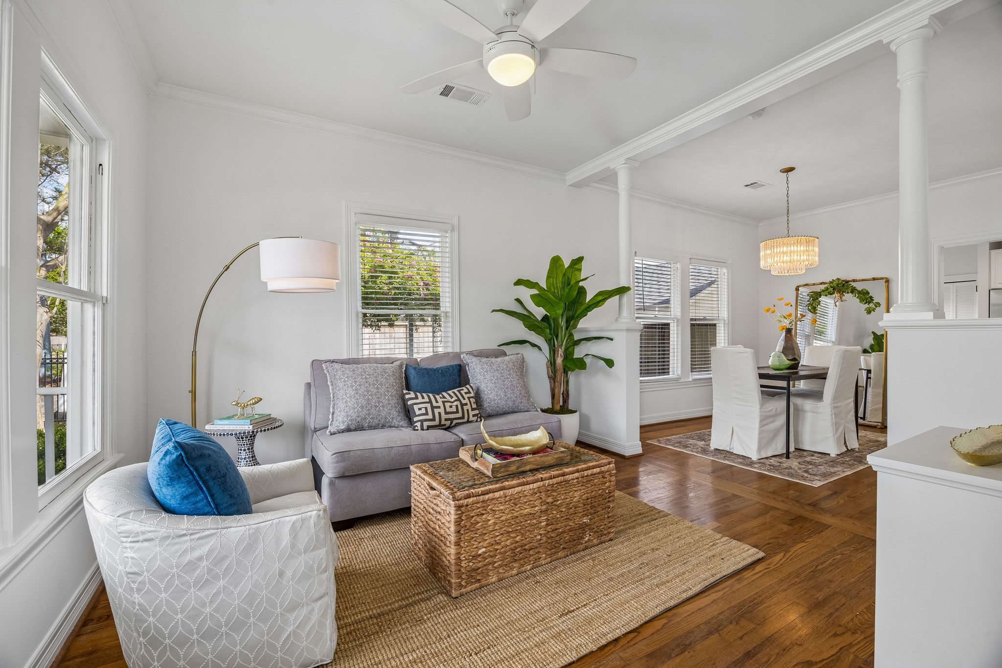 812 West 13th Street Houston, TX 77008 - Photo 12 of 29 This photo showcases a bright, open-concept living and dining area with hardwood floors. The living room features a cozy seating arrangement with a modern floor lamp, while the dining area has an elegant chandelier and seating for six. Large windows provide ample natural light, and a ceiling fan adds comfort.
