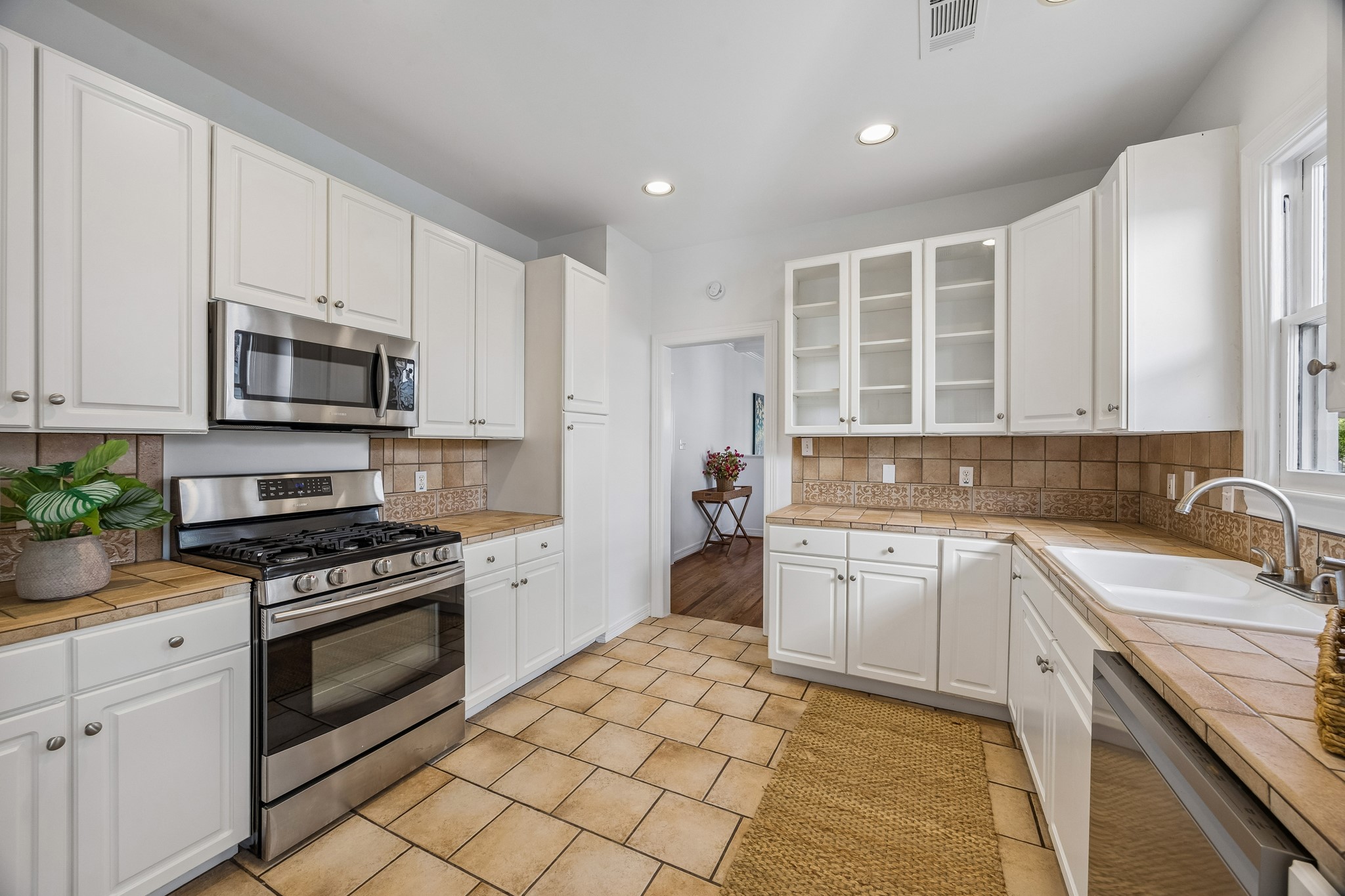 812 West 13th Street Houston, TX 77008 - Photo 14 of 29 This kitchen features white cabinetry, a stainless steel oven and microwave, and a tiled backsplash and countertop. It has ample natural light, a double sink, and a tiled floor, offering a clean and modern look.