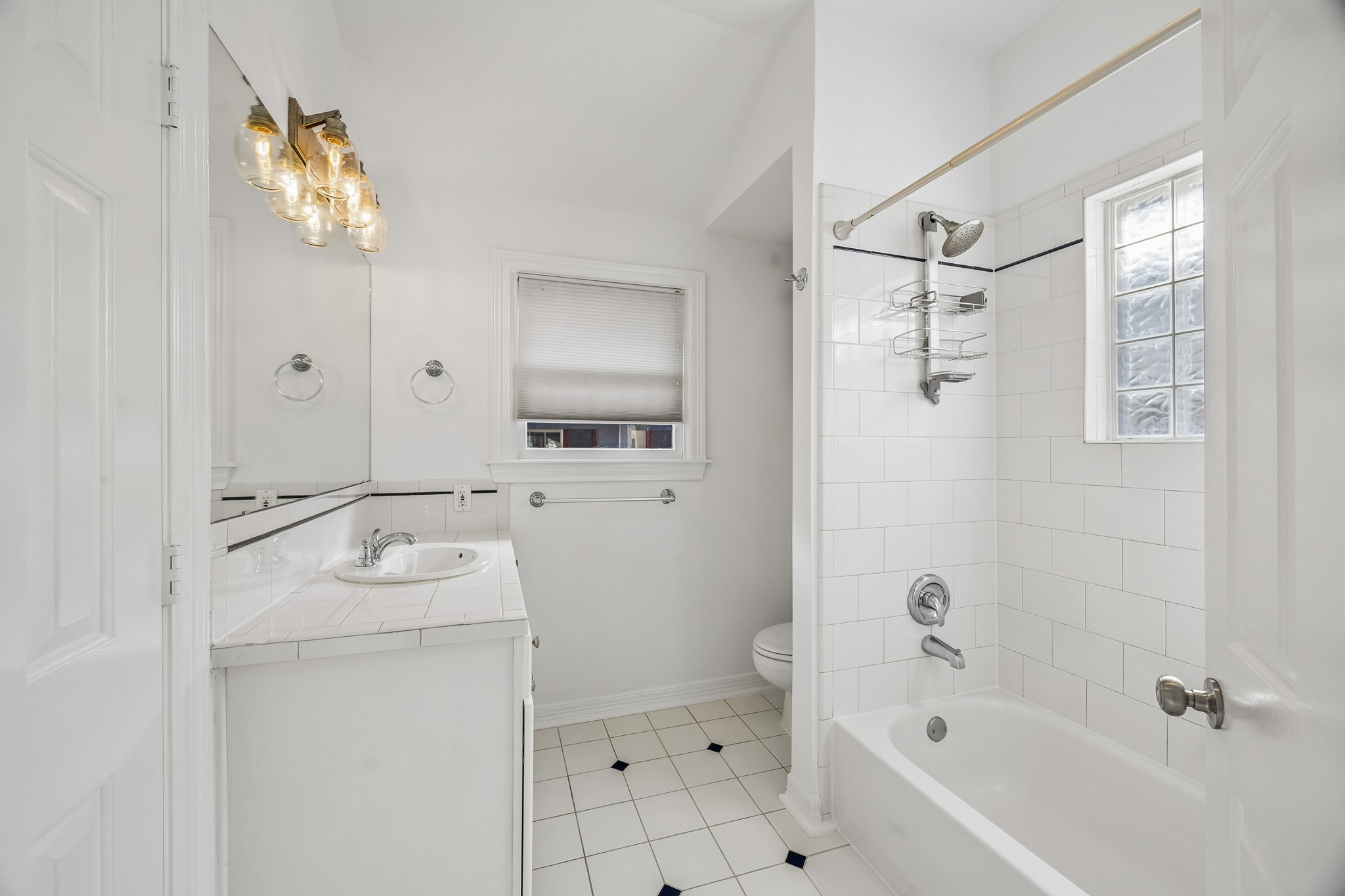 812 West 13th Street Houston, TX 77008 - Photo 17 of 29 Bright and clean bathroom featuring white tiles, a bathtub with shower, and a vanity with ample lighting. The space includes a window for natural light and a simple, elegant design.