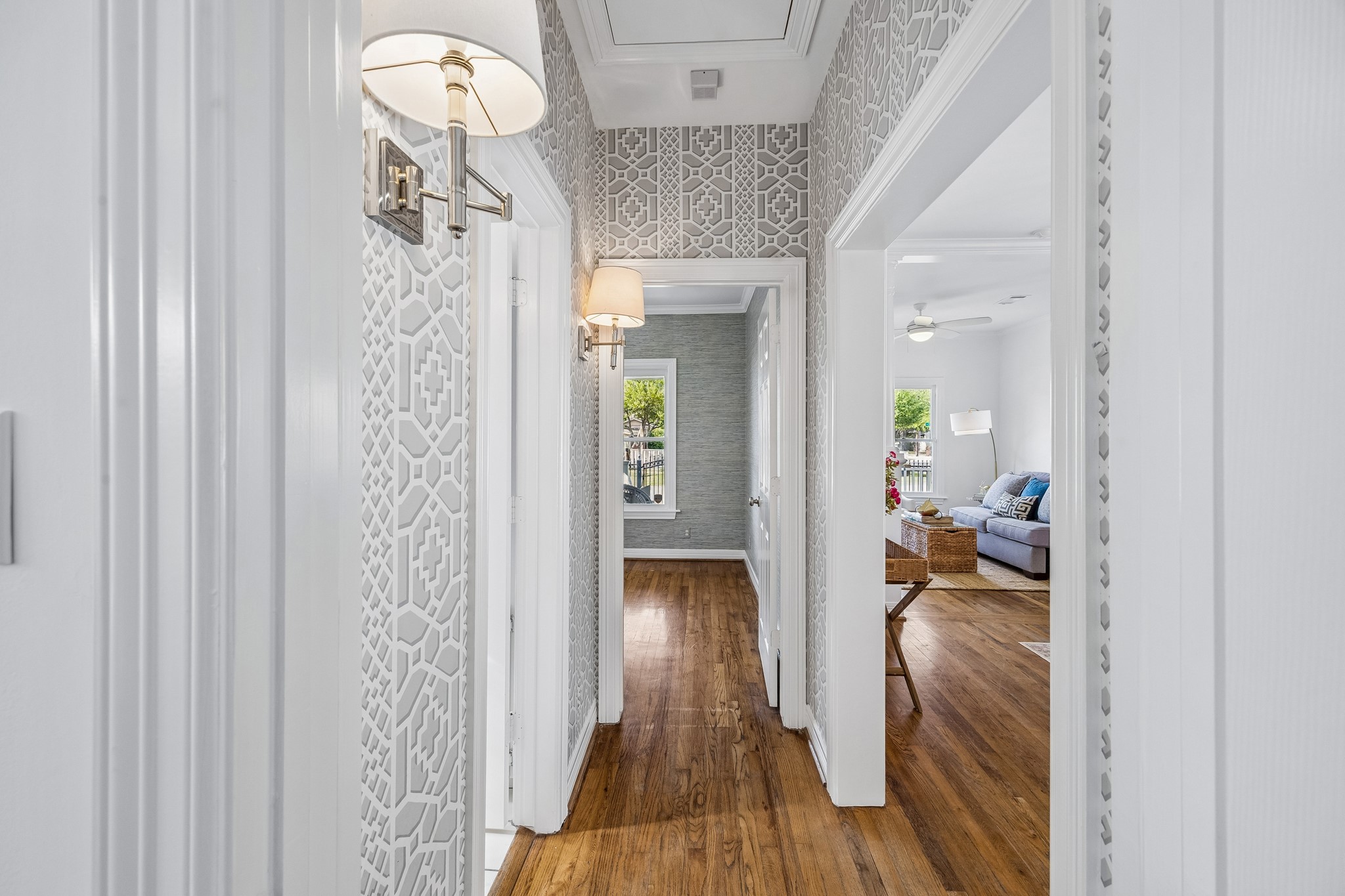 812 West 13th Street Houston, TX 77008 - Photo 19 of 29 This photo showcases a bright hallway with patterned wallpaper, elegant wall sconces, and gleaming hardwood floors, leading into a cozy, well-lit living room.