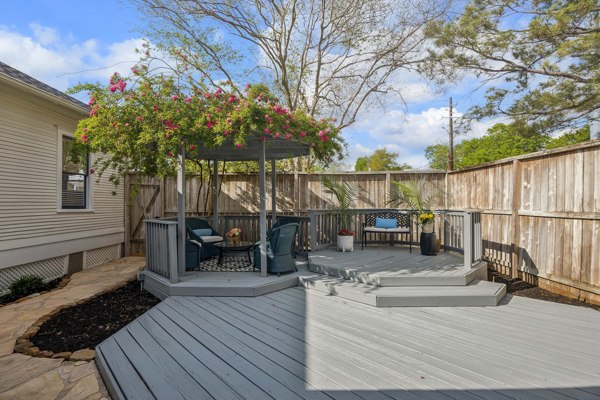 812 West 13th Street Houston, TX 77008 - Photo 23 of 29 Charming backyard with a spacious gray deck featuring a cozy seating area under a pergola adorned with flowering vines. The area is fenced for privacy and enhanced with potted plants, creating a serene outdoor retreat.
