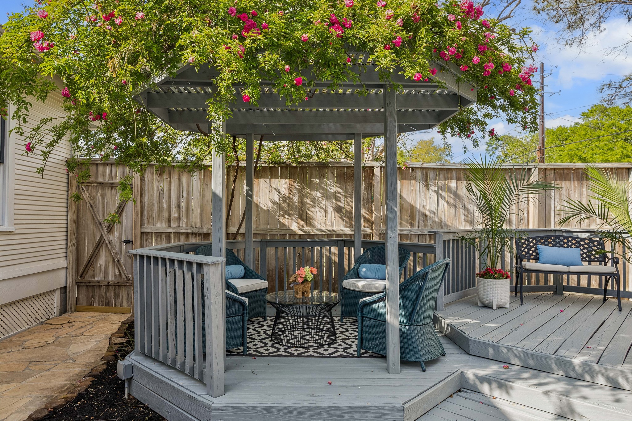 812 West 13th Street Houston, TX 77008 - Photo 24 of 29 This inviting outdoor space features a charming gazebo with lush foliage and vibrant flowers. It includes comfortable seating on a patterned rug, perfect for relaxing. The wooden deck extends to a bench with plants, creating a serene and private retreat.