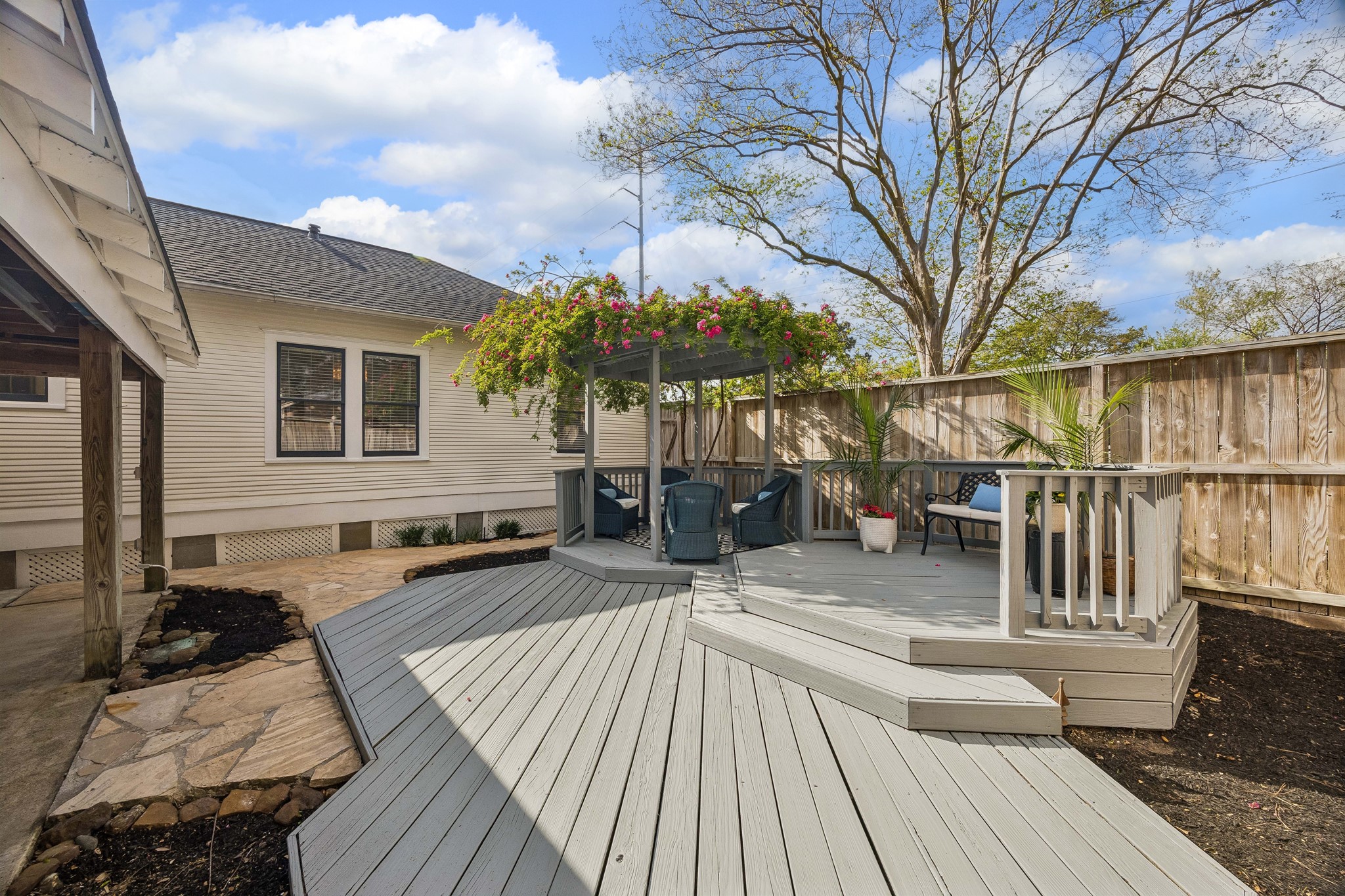 812 West 13th Street Houston, TX 77008 - Photo 25 of 29 This photo showcases a charming backyard with a spacious wooden deck, featuring a pergola adorned with flowering plants. There's comfortable seating and potted greenery, perfect for relaxation and entertaining. The area is enclosed by a wooden fence, providing privacy and a cozy atmosphere.