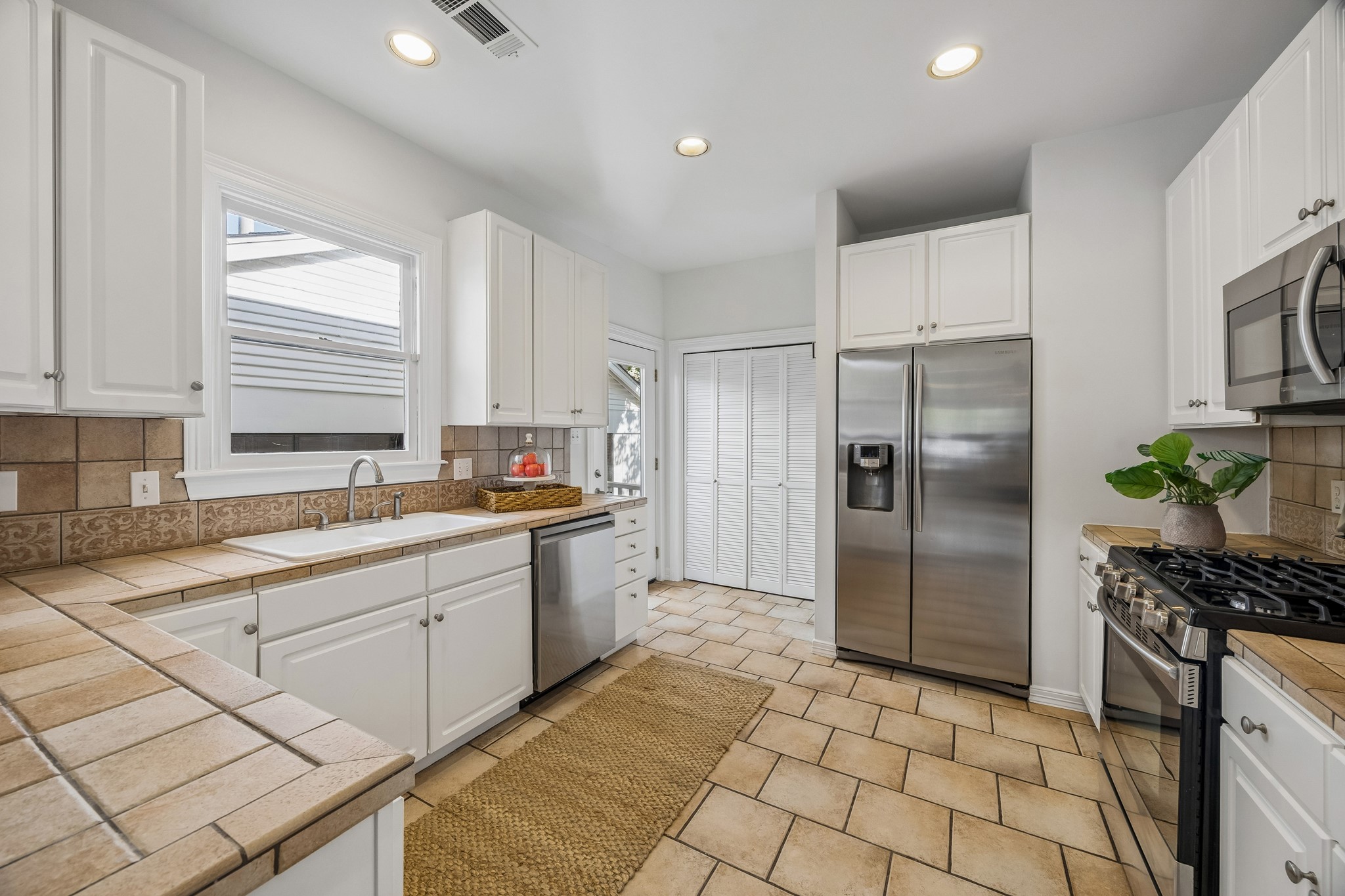 812 West 13th Street Houston, TX 77008 - Photo 4 of 29 This kitchen features bright white cabinetry, stainless steel appliances, and tile countertops. It has a cozy, inviting feel with plenty of natural light and a functional layout.