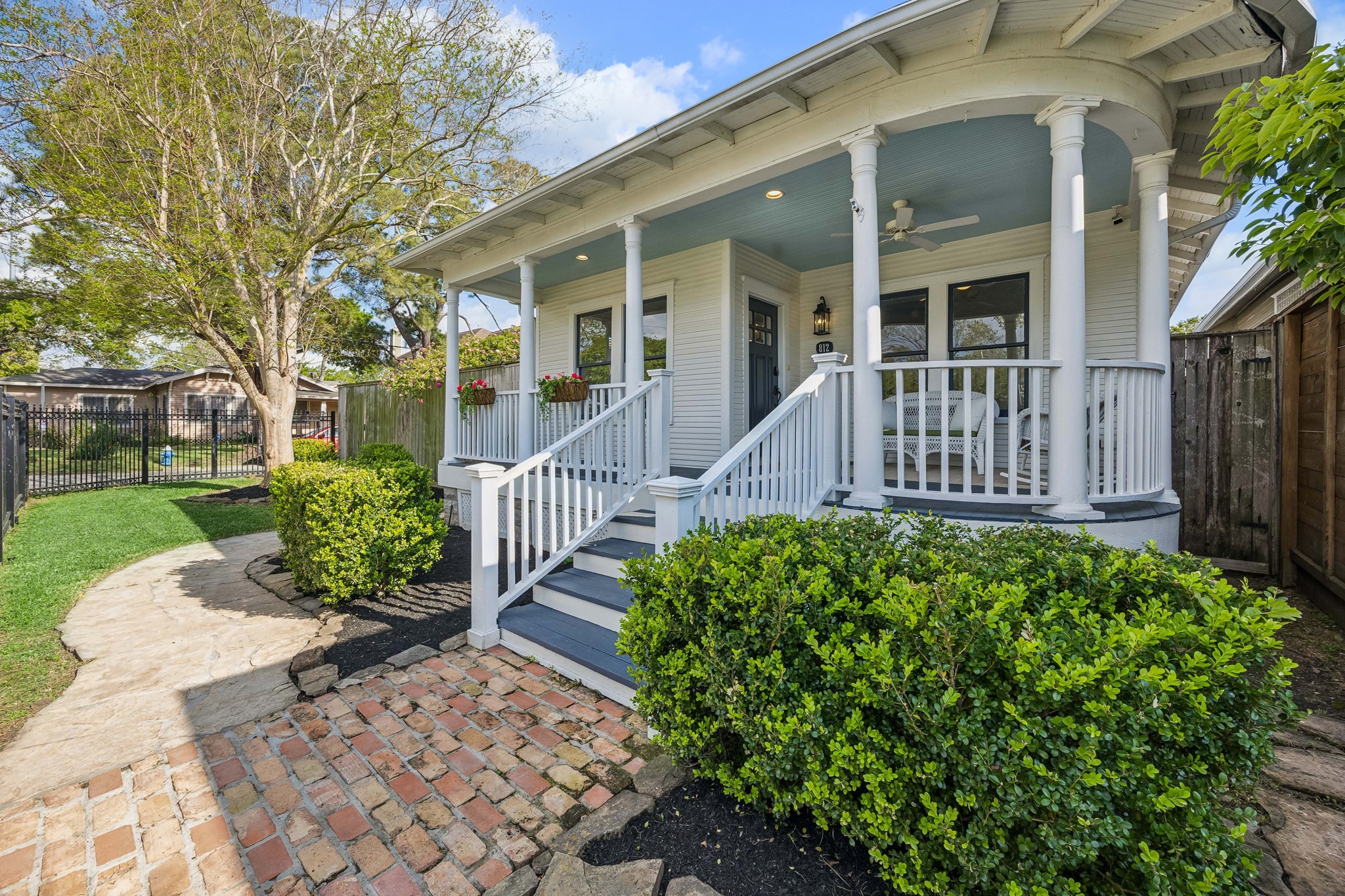 812 West 13th Street Houston, TX 77008 - Photo 5 of 29 Charming home with a welcoming front porch featuring white railings and columns. The yard is beautifully landscaped with a brick and stone walkway, lush greenery, and mature trees, creating an inviting outdoor space.