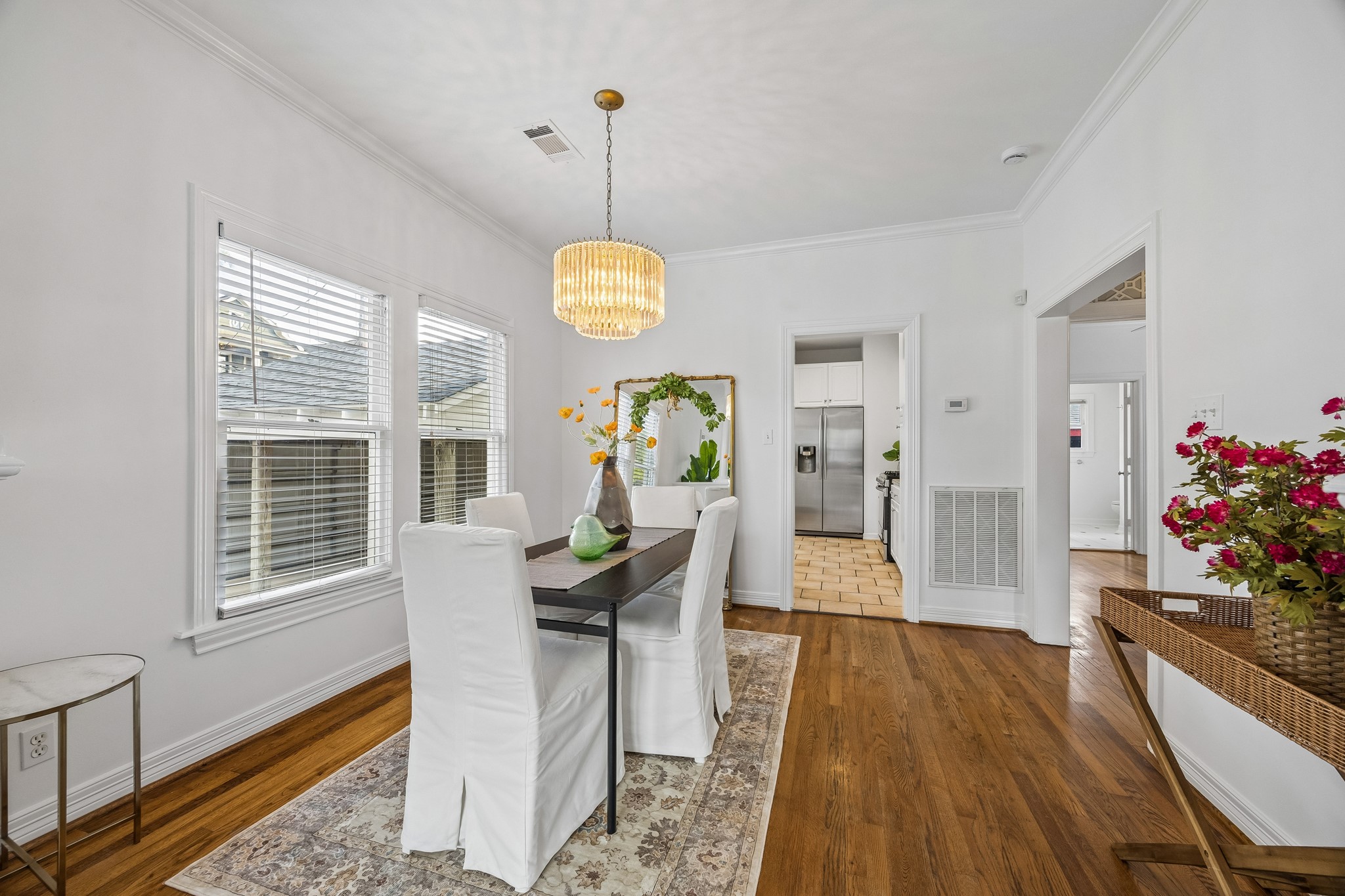 812 West 13th Street Houston, TX 77008 - Photo 10 of 29 Bright dining area with hardwood floors, featuring a modern chandelier and ample natural light from multiple windows. The space includes a sleek dining table, white slipcovered chairs, and connects to a kitchen with stainless steel appliances.