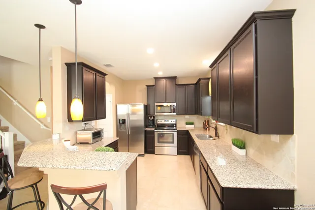 a kitchen with stainless steel appliances kitchen island granite countertop a refrigerator a stove and a sink with wooden floor