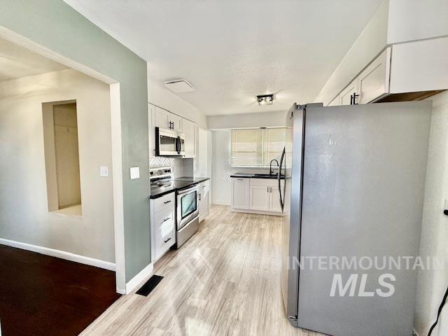 1139 Webster Street Clarkston, WA 99403 - Photo 13 of 34 Kitchen with stainless steel appliances, white cabinets, light wood-style floors, and dark countertops