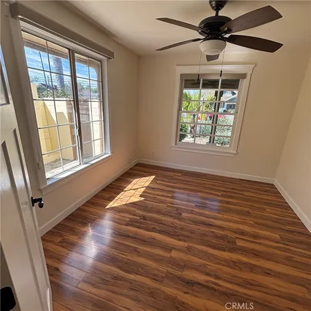 an empty room with wooden floor fan and windows