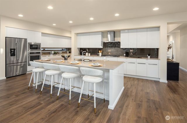 a kitchen with stainless steel appliances granite countertop a stove top oven a sink dishwasher a refrigerator and white cabinets with wooden floor