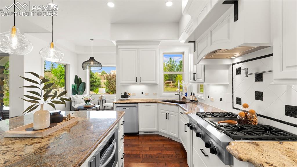 13625 Random Ridge View Colorado Springs, CO 80921 - Photo 12 of 50 Kitchen featuring light stone counters, appliances with stainless steel finishes, premium range hood, pendant lighting, and white cabinetry