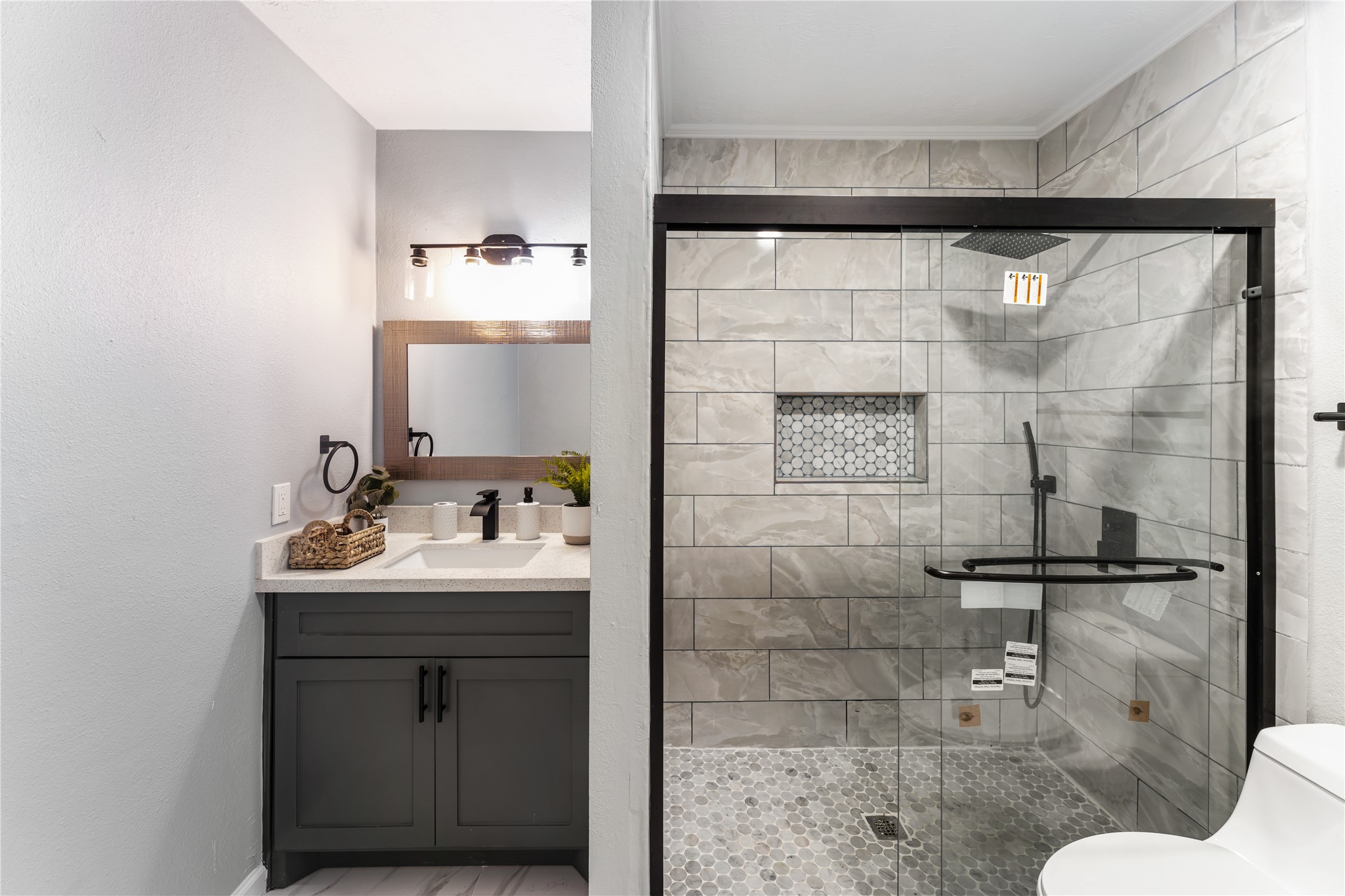 9425 Fondren Road Houston, TX 77074 - Photo 25 of 29 The secondary bathroom features a modern design with a spacious glass-enclosed shower showcasing stylish tile work and a built-in niche. The vanity area includes a sleek sink with contemporary fixtures, set against a neutral-tone wall.