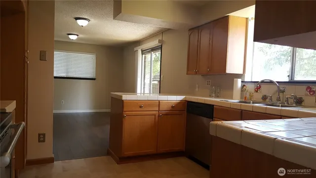 a kitchen with stainless steel appliances granite countertop a refrigerator a sink dishwasher a stove and a dining table with wooden cabinet