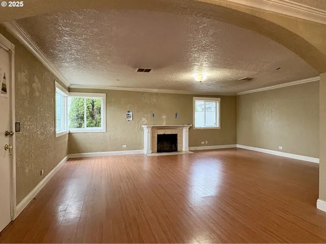 an empty room with wooden floor fireplace and windows