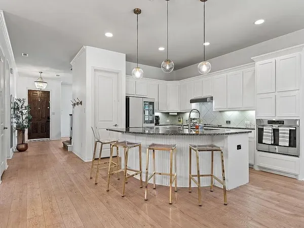 a kitchen with stainless steel appliances granite countertop a sink a stove a refrigerator and white cabinets with wooden floor