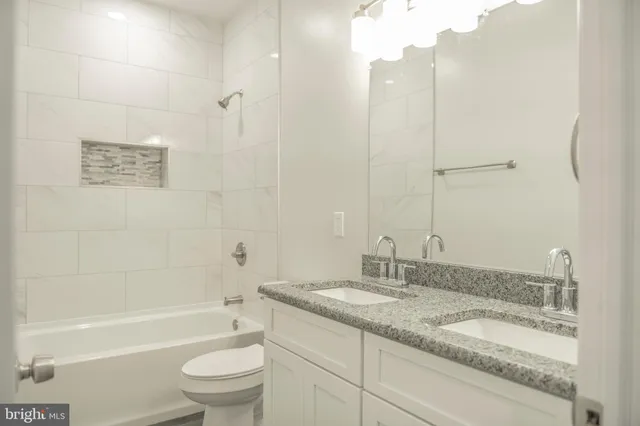 a bathroom with a granite countertop double vanity sink a mirror and a toilet