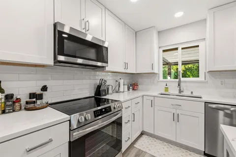 a kitchen with stainless steel appliances white cabinets granite counter tops and a window