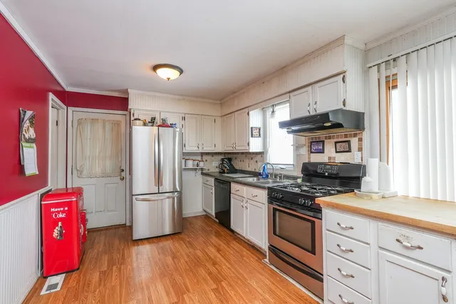 a kitchen with stainless steel appliances granite countertop a refrigerator a stove top oven a sink dishwasher and white cabinets with wooden floor
