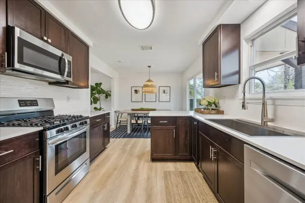 a kitchen with stainless steel appliances granite countertop a stove top oven a sink dishwasher and a microwave oven with large wooden cabinets