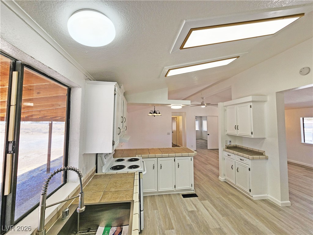 1860 West Wilson Road Pahrump, NV 89048 - Photo 12 of 16 Kitchen featuring lofted ceiling, electric range, white cabinets, light wood-type flooring, and a peninsula