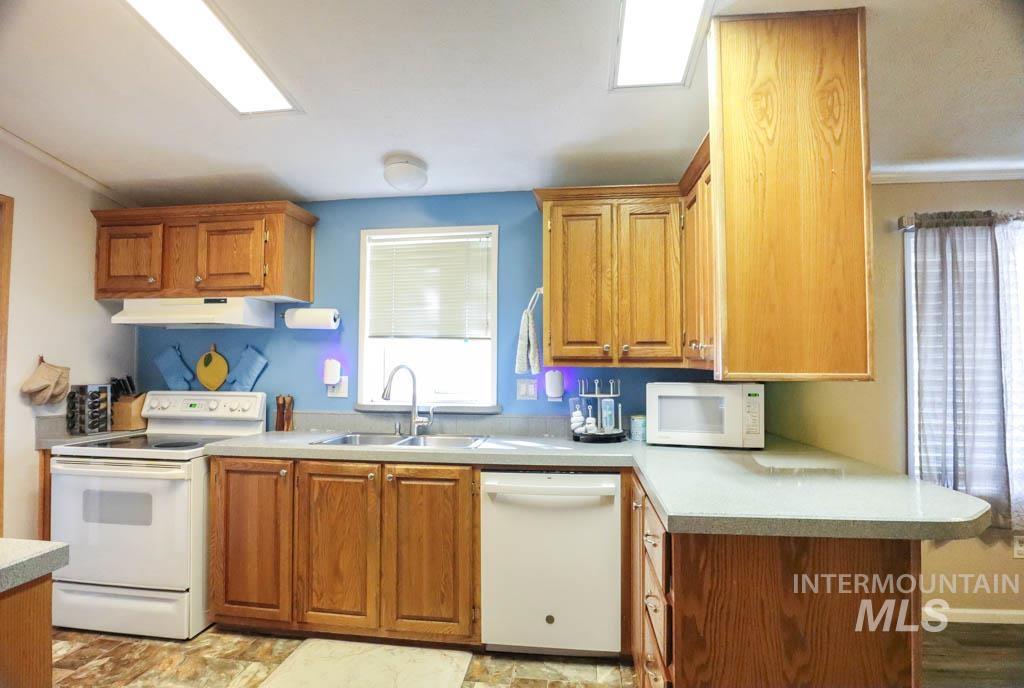 815 Eaton Road Weiser, ID 83672 - Photo 15 of 50 Kitchen with white appliances, light countertops, brown cabinets, and under cabinet range hood