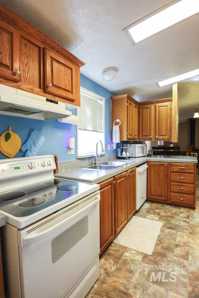 815 Eaton Road Weiser, ID 83672 - Photo 18 of 50 Kitchen featuring white appliances, brown cabinets, under cabinet range hood, stone finish floors, and light countertops