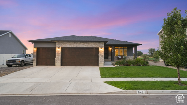 Prairie-style home with stone siding, covered porch, a front lawn, an attached garage, and driveway