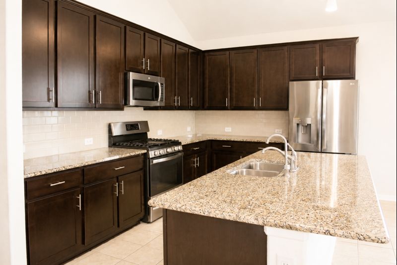 693 Durian Loop Buda, TX 78610 - Photo 9 of 27 A well-appointed culinary space featuring dark wood cabinetry and polished granite countertops.