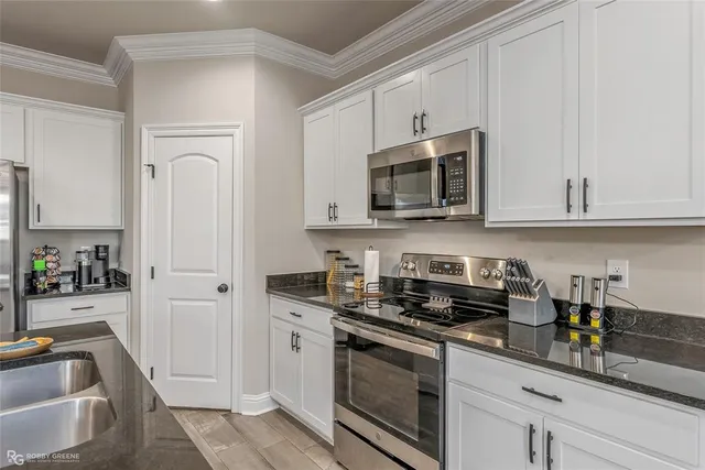 a kitchen with granite countertop white cabinets stainless steel appliances a sink and wooden floor