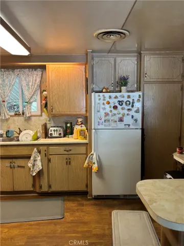 a kitchen with stainless steel appliances a white refrigerator a sink a stove and white cabinets with wooden floor