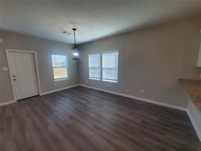 an empty room with wooden floor chandelier and windows