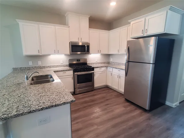 a kitchen with granite countertop a refrigerator a sink and white cabinets