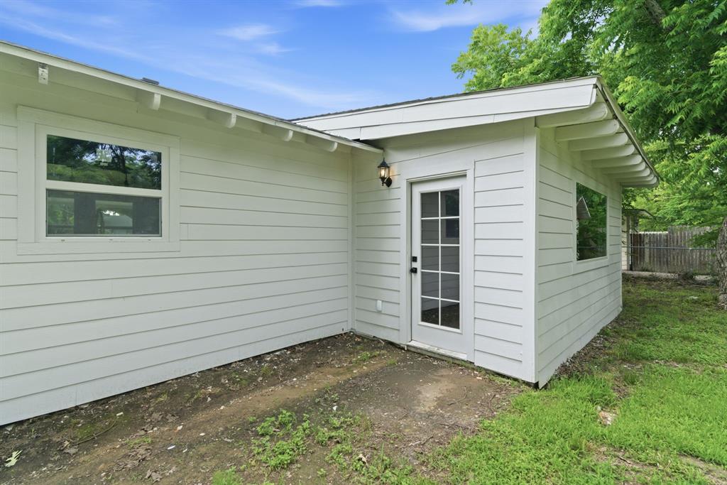 507 Country Club Road Cleburne, TX 76033 - Photo 33 of 39 White horizontal siding exterior featuring a glass-paned door, exterior lighting fixture, and multiple windows with white trim