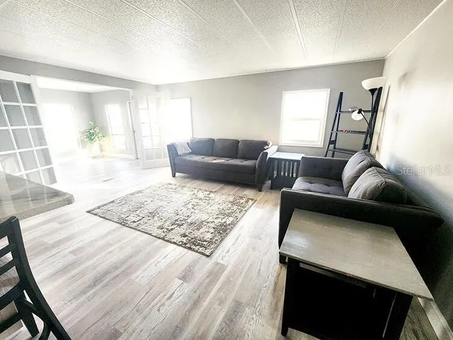 a living room with stainless steel appliances furniture a rug and a kitchen view