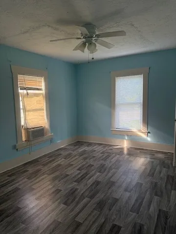 an empty room with wooden floor fan and windows