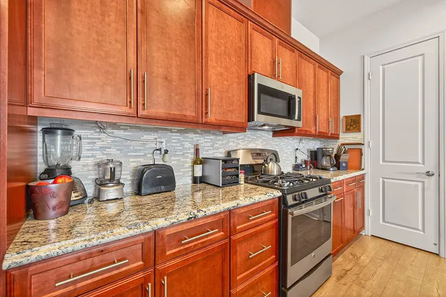 a kitchen with stainless steel appliances granite countertop a stove top oven a sink dishwasher and white cabinets with wooden floor