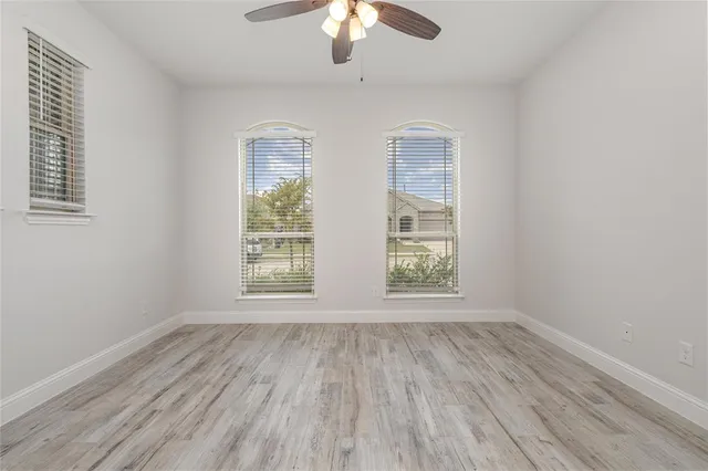an empty room with wooden floor chandelier fan and windows