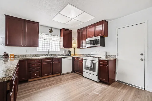 a kitchen with stainless steel appliances granite countertop wooden cabinets a stove top oven a sink and dishwasher with wooden floor