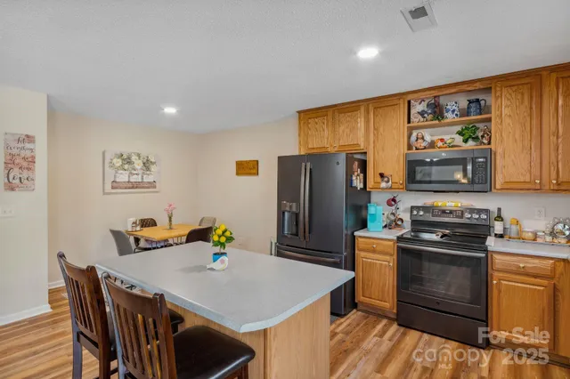 a kitchen with stainless steel appliances granite countertop a refrigerator a stove a sink a dining table and chairs with wooden floor